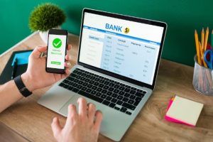 Pessoa usando simultaneamente um smartphone com a mensagem “Money Received” e um notebook com extrato bancário na tela, ilustrando o processo de recebimento e controle financeiro. A imagem representa como funciona o empréstimo pessoal com débito em conta de forma prática e automatizada.