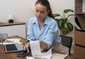 Mulher analisando contas e boletos com calculadora ao lado do notebook, demonstrando preocupação com o risco de atrasar parcelas do empréstimo pessoal.