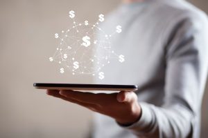 Pessoa segurando um tablet com ícones de cifrões conectados em rede digital, representando a inovação e a tecnologia no mercado de crédito pessoal.