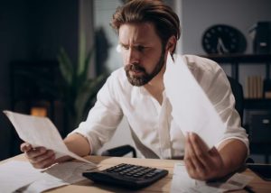 Homem concentrado analisando documentos financeiros e usando uma calculadora em seu escritório, representando a avaliação de opções de refinanciamento de empréstimo pessoal para melhorar o planejamento financeiro.