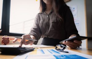 Mulher em ambiente de trabalho usando simultaneamente calculadora, celular e anotações em papel, simbolizando o uso de simuladores de empréstimo pessoal para planejamento financeiro detalhado.