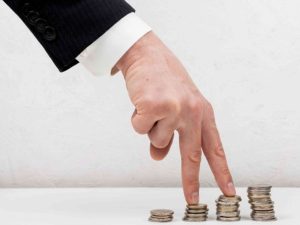 Mão de homem em terno tocando pilhas crescentes de moedas, simbolizando o impacto das taxas abusivas em contratos de empréstimo pessoal sobre o orçamento do consumidor.